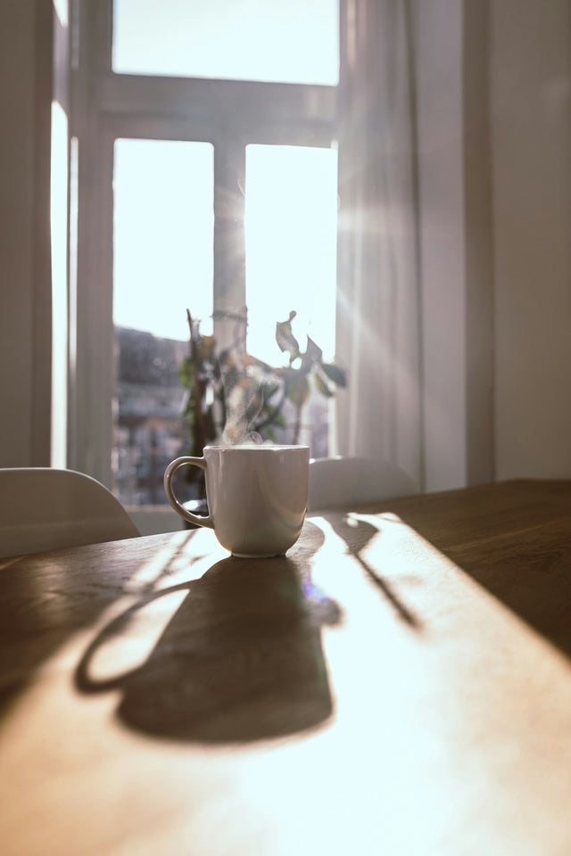 Dampende mok op een houten tafel voor een zonnig raam